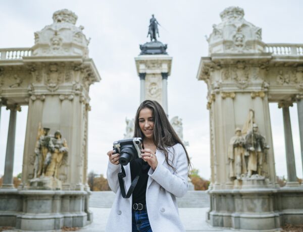 Femme souriante avec une caméra debout devant le monument Alfonso XII dans le parc El Retiro, Madrid